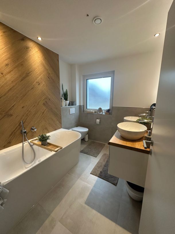 Helles Bad mit Badewanne, Akzentwand in Holzoptik im Fischgrätmuster und Doppelwaschtisch