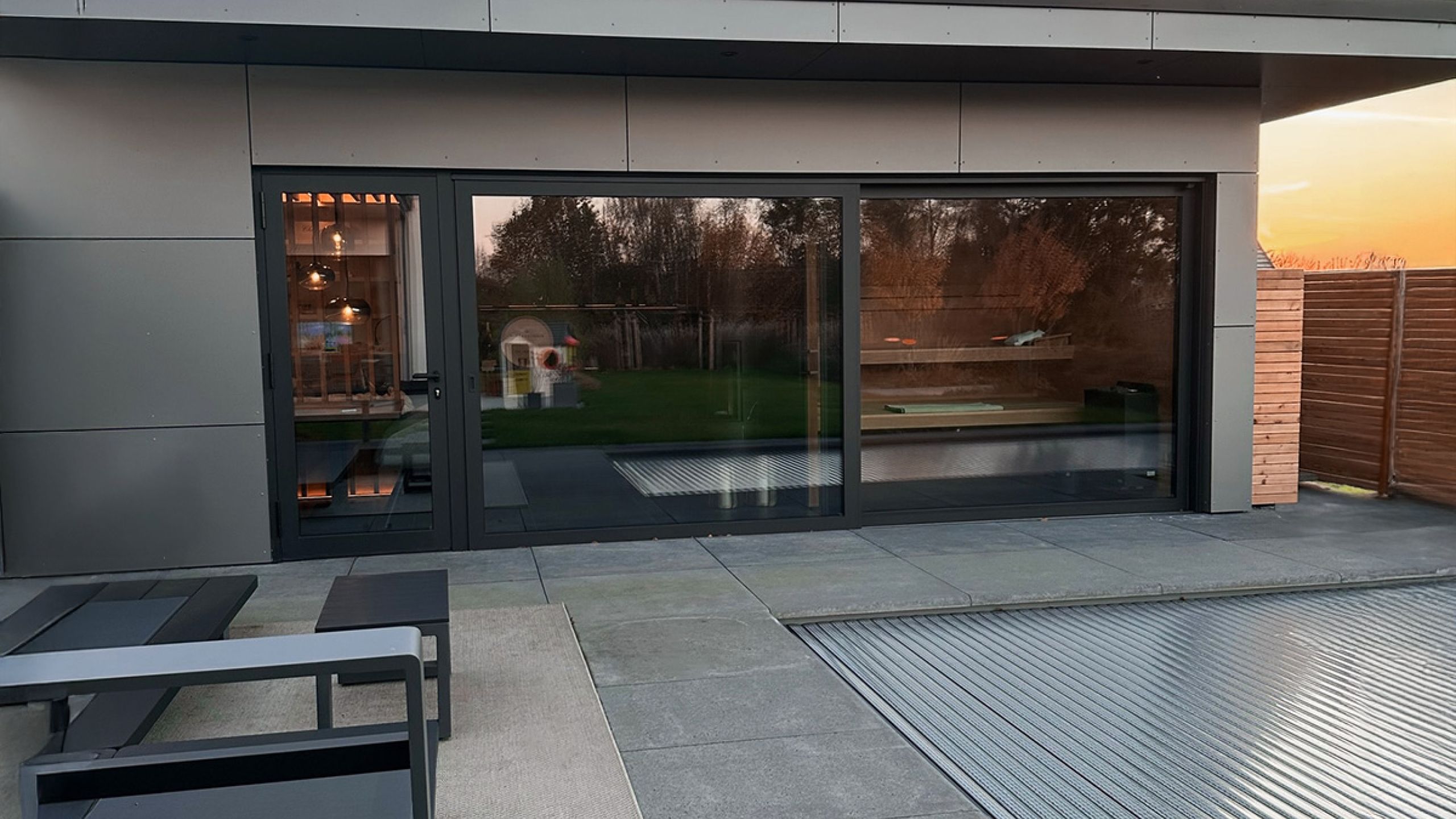 Dachterrasse mit großformatigen grauen Terrassenplatten vor bodentiefen Fenstern bei Sonnenuntergang