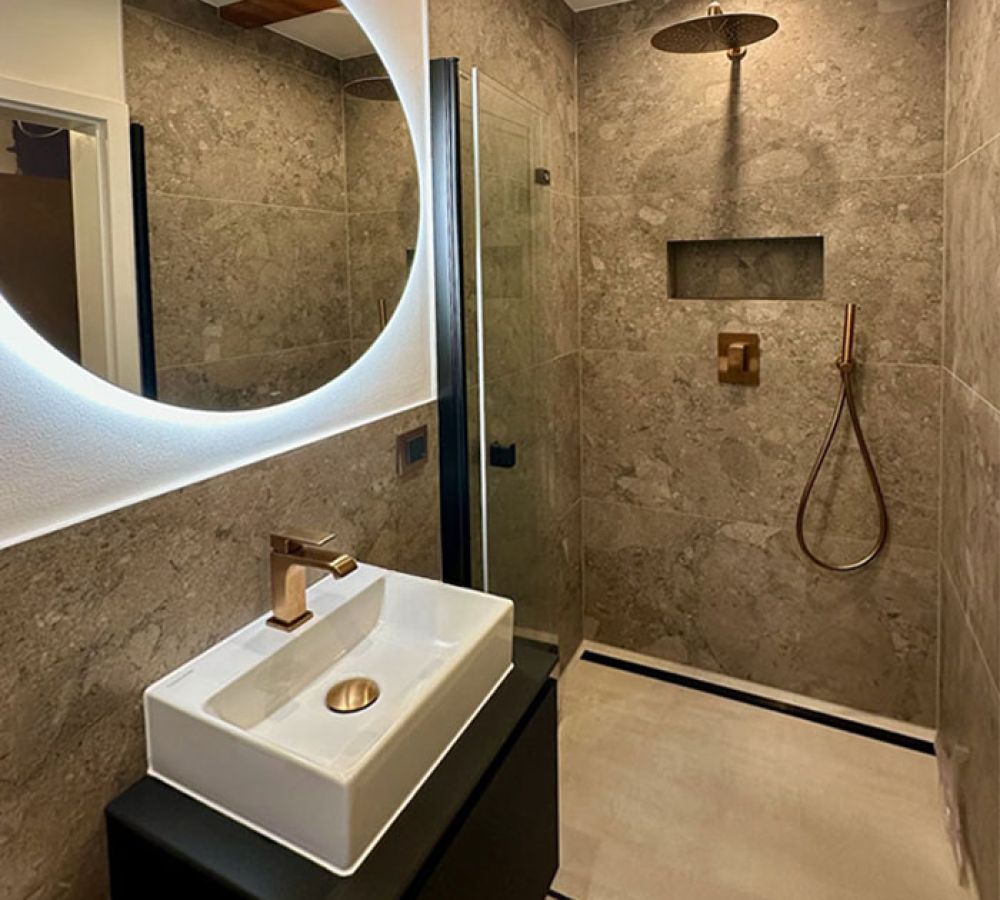 Duschbad mit Terrazzo-Steinoptik, rundem beleuchtetem Spiegel, Aufsatzbecken und bodengleicher Dusche