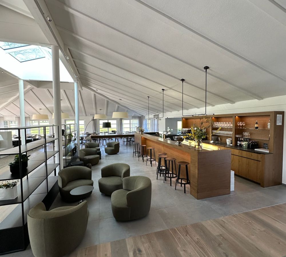 Lounge mit Bar unter hellem Dach, Boden aus großformatigen grauen Fliesen und Holzdielenbereich