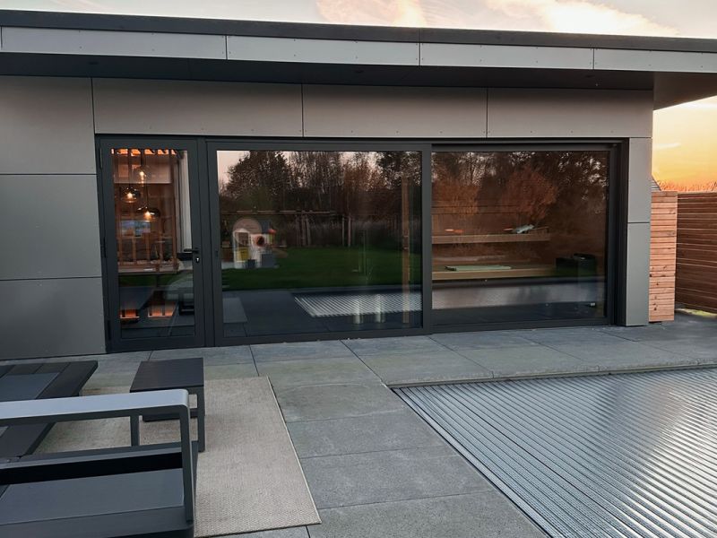 Dachterrasse mit großformatigen grauen Terrassenplatten vor bodentiefen Fenstern bei Sonnenuntergang