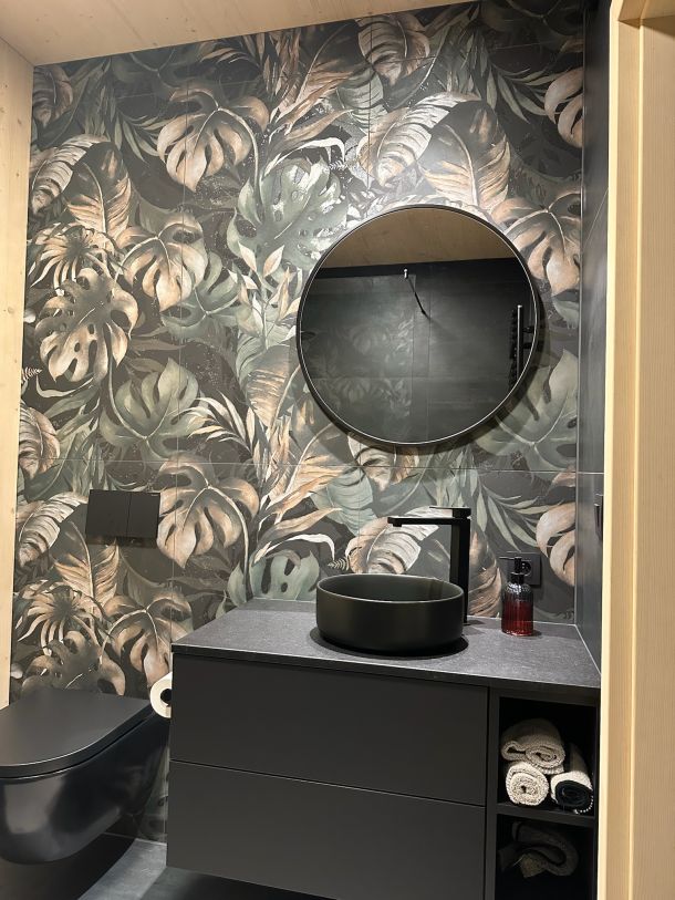 Gäste-WC mit Wandfliesen im dunklen Dschungel-Blätterdekor, rundem Spiegel und schwarzem Aufsatzbecken