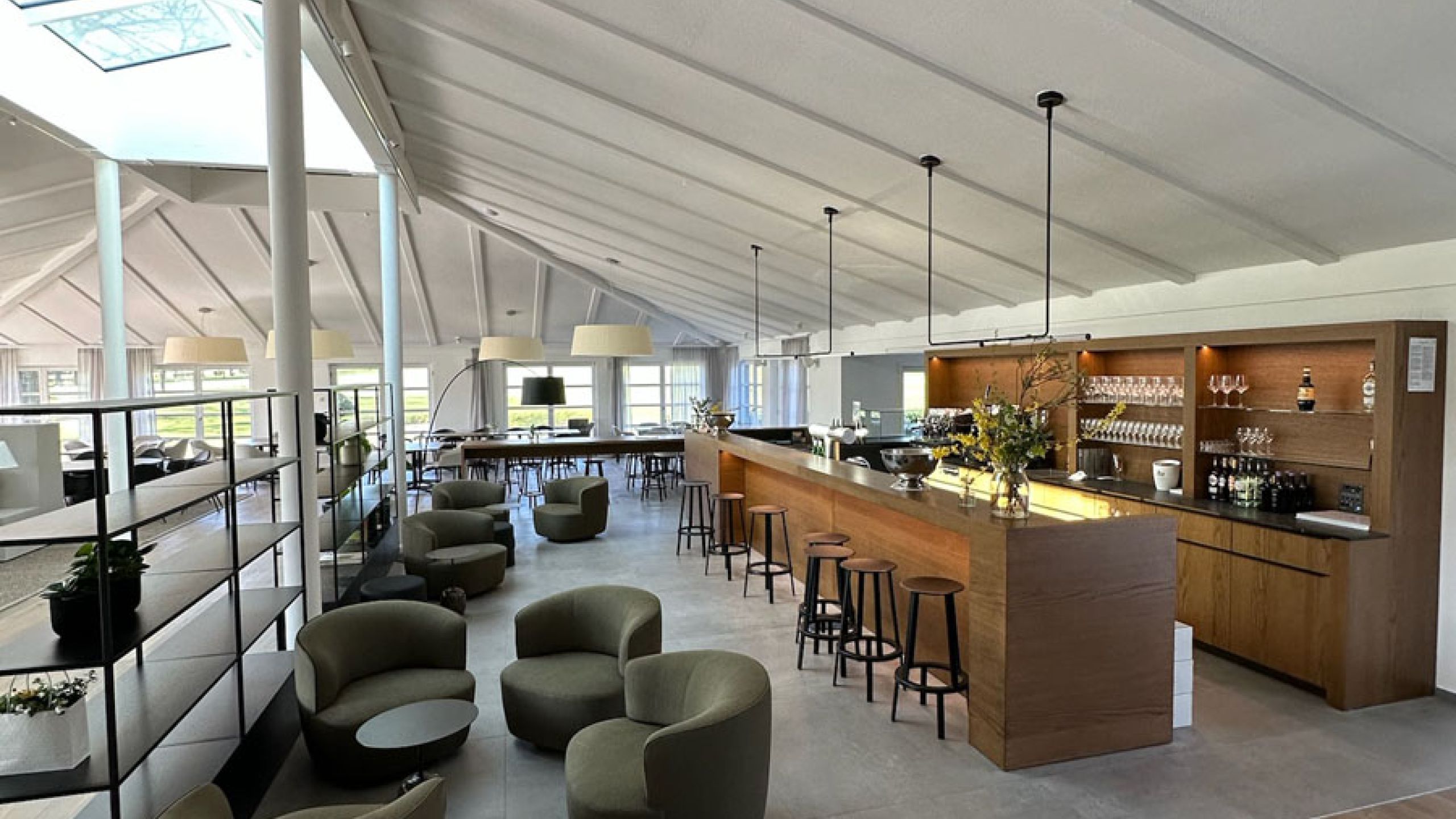 Lounge mit Bar unter hellem Dach, Boden aus großformatigen grauen Fliesen und Holzdielenbereich