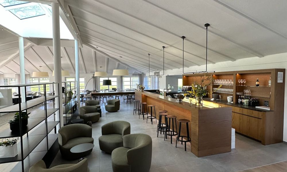 Lounge mit Bar unter hellem Dach, Boden aus großformatigen grauen Fliesen und Holzdielenbereich