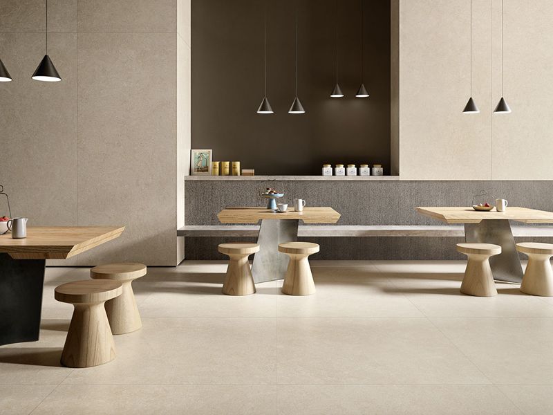 Café mit Holztischen und Hockern auf großformatigen hellbeigen Boden- und Wandfliesen in Steinoptik