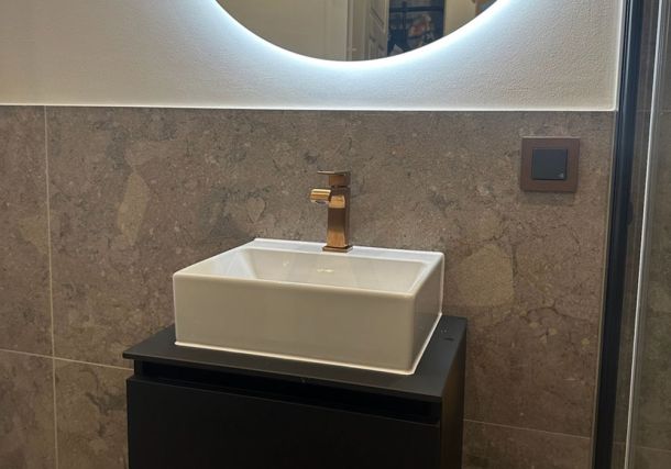 Aufsatzwaschbecken mit kupferfarbenem Wasserhahn vor Wandfliesen in Terrazzo-Steinoptik