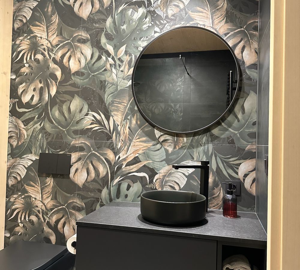 Gäste-WC mit Wandfliesen im dunklen Dschungel-Blätterdekor, rundem Spiegel und schwarzem Aufsatzbecken