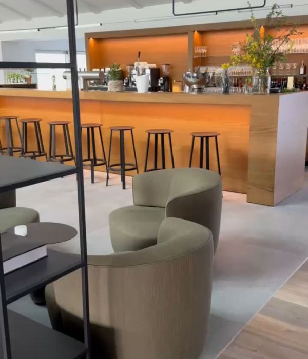 Bartheke mit Holzfront und Barhockern, davor Sessel auf hellgrauen Großformatfliesen in Betonoptik