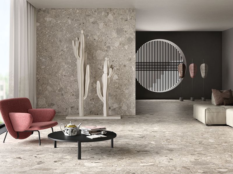 Wohnraum mit großformatigen Boden- und Wandfliesen in Terrazzo-Optik, rotem Sessel und Couchtisch