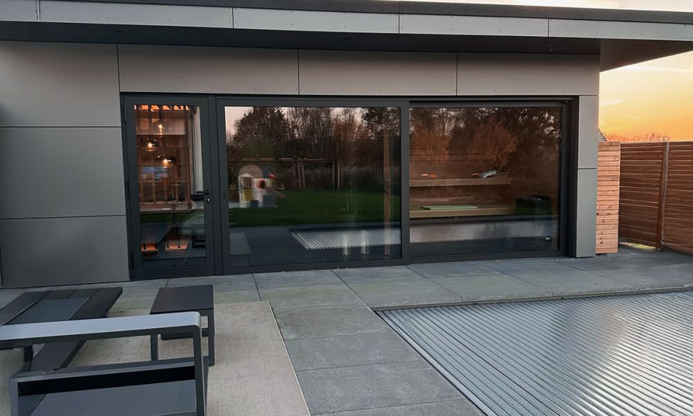 Dachterrasse mit großformatigen grauen Terrassenplatten vor bodentiefen Fenstern bei Sonnenuntergang