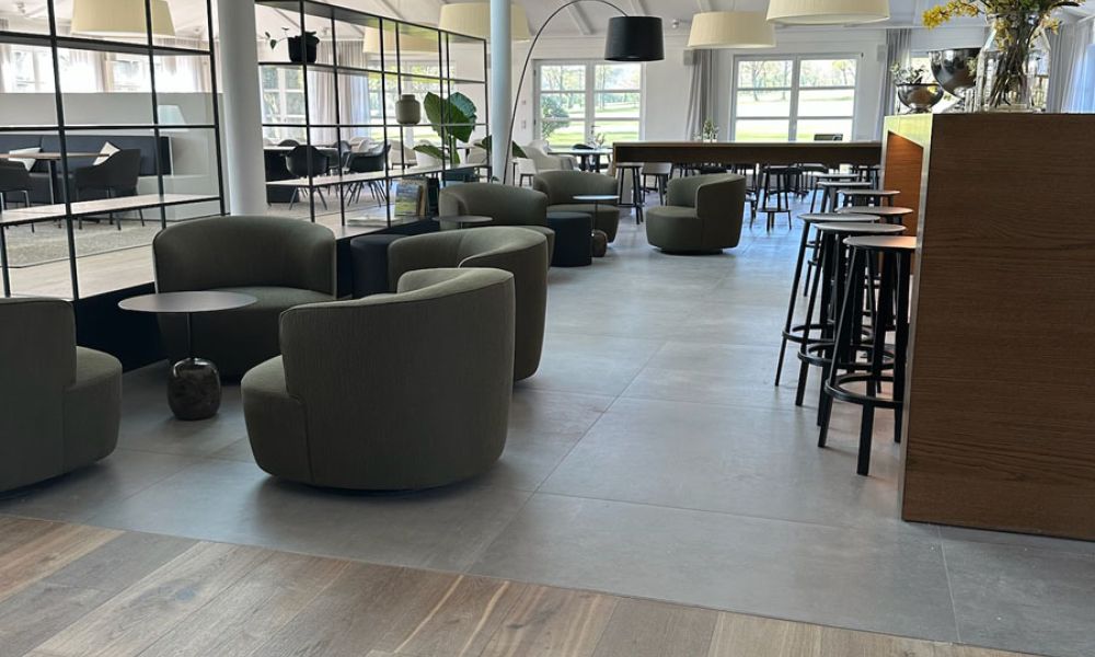 Lounge mit hellgrauen Großformatfliesen in Betonoptik, Holzboden im Vordergrund, Sesseln und Bartheke