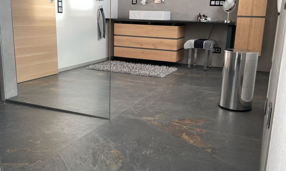Großzügiges Bad mit großformatigen dunklen Bodenfliesen in Schieferoptik, Glasduschwand und Waschtisch