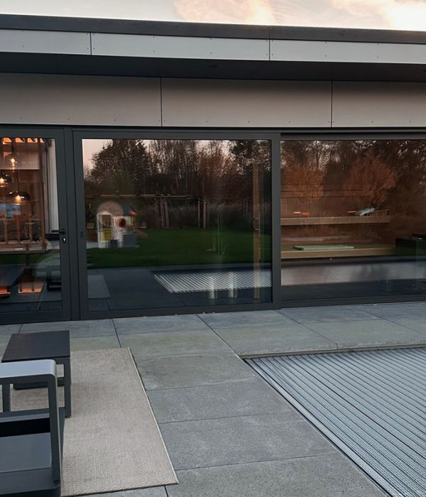 Dachterrasse mit großformatigen grauen Terrassenplatten vor bodentiefen Fenstern bei Sonnenuntergang