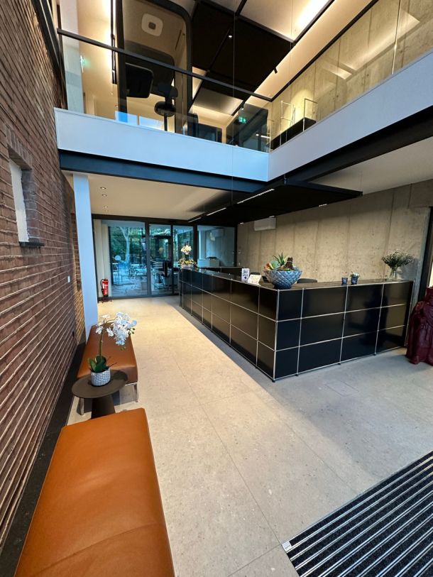 Foyer mit Klinkerwand, Empfangstheke und hellem Boden aus großformatigen Fliesen in Terrazzo-Optik